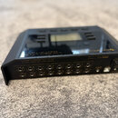Černý elektronický přístroj s LCD displejem na horní straně. Na přední hraně je nápis „Live Player LP16 is Track Player and USB Interface“, označení…