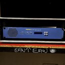 Modré rackové zařízení s nápisem MIDAS DL151 audio system I/O umístěné v hliníkovém přepravním kufru. Na předním panelu jsou vidět kontrolky, displej…