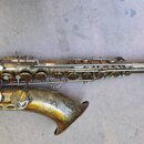 Mosazný saxofon s výraznou patinou a viditelným opotřebením povrchového lakování. Nástroj je zobrazen v celku z profilu, bez připojeného mouthpiece.…