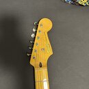Fotka zachicuje hlavu a horní část hmatníku elektrické kytary v přirozené dřevěné barvě. Na hlavě je vidět nápis Squier by Fender a STRATOCASTER®. Po…
