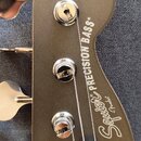 Hlava basové kytary v šedé barvě s kovovými ladičkami. Na povrchu je bílý nápis Squier by Fender PRECISION BASS®. V horní části hlavy je umístěno mal…