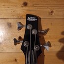 Černá hlava basové kytary s nápisy "gio Ibanez" a pod nimi "SOUNDGEAR". Jsou na ní vidět čtyři chromované ladičky a struny. Povrch je hladký, bez vid…