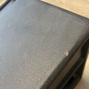 Detailní záběr na horní hranu a povrch černého zařízení s texturovaným povrchem. Na pravé hraně je viditelné drobné odřesení laku. Žádné značky ani n…