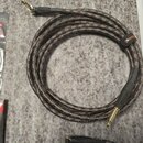 Svinutý kytarový kabel s pleteným obalem v tmavé barvě s oranžovými proužky. Na kabelu je černý suchý spoj s oranžovým nápisem Roland a na konektorec…