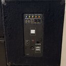 Zadní strana černého reproduktoru potaženého plstěvým materiálem. V horní části je ovládací panel s knoflíky označenými jako MIC VOL, BASS, TREBLE, S…
