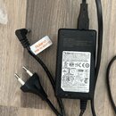 Černý síťový adaptér značky Roland. Na štítku je uveden model PSB-1U ADAPTOR a řada certifikačních značek včetně NOM, CE a JET. Adaptér má standardní…