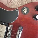 Detail červené elektrické kytary s černým plechtrátem. Na těle je přepínač s nápisy TREBLE a RHYTHM a dva bílé otočné knoflíky s nápisem VOLUME. Povr…