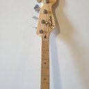 Fotografie zachycuje hmatník a hlavu basové kytary z přírodního světlého dřeva. Na hlavě je čitelné logo Fender a nápis JAZZ BASS. Nástroj má čtyři l…