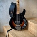 Elektrická basová kytara s tělem v černé barvě s přechodem do hnědé (sunburst) a černým plechtem. Na těle jsou vidět tři ovládací knofíky a kovový mo…