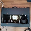 Černý kytarový kombo zesilovač s otevřeným zadním panelem. Uvnitř jsou vidět dvě elektronky, transformátor s nečitelným nápisem a reproduktor. Skříň…