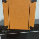 Kvadratický kytarový zesilovač nebo box s oranžovým texturovaným povrchem. Rohy jsou chráněny černými plastovými nárožníky a boky zdobí dva svislé če…