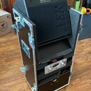 Černý transportní case s kovovými hranami a zámky, v němž je umístěn černý kompaLní zesilovač s nápisem Compact 80 pro a quad channel pro line. Na př…
