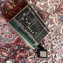 Stříbrný mikro synthesizer s černým ovládacím panelem a posuvníky. Na přední straně je zelený nápis BASS MICRO SYNTHESIZER a bílé texty ELECTRO HARMO…
