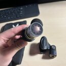 Detailní pohled na horní část mikrofonu s kovovou mřížkou. Na těle je viditelný nápis XODIX MADE IN USA. V pozadí jsou rozmazaná černá klaviatura, če…