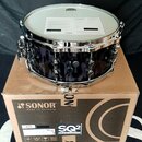 Černý buben s chromovaným obručováním a ladicími šrouby, položený na kartónovém balení. Na krabici je vidět logo SONOR s nápisem Made in Germany a oz…