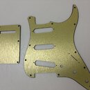Zlatavý kovový pickguard a doprovodná krytka pro elektrickou kytaru. Povrch obou dílů má jemný broušený vzhled s viditelnými lineárními rýhami. Na dí…