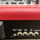 Detail zadní strany červeného hudebního zařízení s černým panelem konektorů. Jsou zde viditelné nápisy MIDI IN, MONITOR IN, CONTROL PEDAL, RIGHT OUT,…