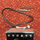 Kromě chromovaného humbuckerového snímače s šesti viditelnými šrouby jsou na červeném podkladu dvě šroubky a jedna pružina. Na bílém kabelu je vidite…