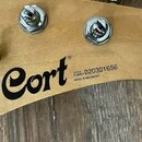 Záběr na zadní stranu hlavy kytary z přírodního dřeva s kovovými ladičkami. Je zde vidět černé logo Cort® a nápisy SERIAL NUMBER 020301656 oraz MADE…