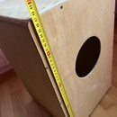 Dřevěná bedna z překážky s kulatým otvorem v přední stěně. K měření rozměrů je přiložen žlutý metr, který ukazuje hodnoty od 20 do 52. Povrch dřeva j…