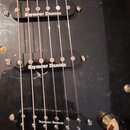 Detail černé elektrické kytary se třemi snímači. Každý ze snímačů má černý kryt s bílým nápisem Seymour Duncan. Povrch kytary vykazuje drobné škrában…