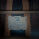 Fotografie zachycuje vnitřní štítek kytary přilepený na dřevěnou desku. Na štítku je modrým tiskem uveden text EST. 1936 HAND CRAFTED, logo v podobě…