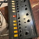 Černý kytarový syntetizátor s nápisem KORG GUITAR SYNTHESIZER. Přední panel obsahuje řadu tlačítek, otočných potenciometrů a posuvníků s popisy jako…