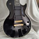 Černá elektrická kytara s tvarem single-cutaway a bílým lemováním hran. Nástroj má dva humbuckery s černými krytymi snímači, čtyři černé ovládací kno…