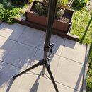 Černý teleskopický stativ s trojnožkou, umístěný na betonové terase. Nástroj je vyroben z kovového materiálu s matným povrchem. Na stativu nejsou vid…