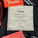 Fotografie zobrazuje dokumenty a příslušenství k hudebnímu nástroji. Uprostřed je Certifikát pravosti s nápisem Fender CERTIFICATE of AUTHENTICITY, m…