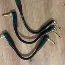 Tři černé audio kabely s úhlovými konektory v tmavě zeleném provedení a zlatými hroty. Na jednom z kabelů je viditelný bílý nápis, ze kterého lze pře…