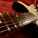 Černá elektrická kytara s hnědým hmatníkem a bílými polohovými značkami. Kytara má světle šedý pickguard s mramorovaným vzorem a tři bílé ovládací kn…