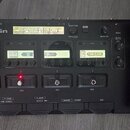 Černý kytarový procesor s nápisem ZOOM G5n Multi-Effects Processor. Zařízení má čtyři LCD displeje, na kterých jsou vidět nápisy TS Drive, DZ, DRU a…