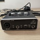 Kompaktní zvuková karta v šedé barvě s kovovým povrchem. Na přední straně je nápis U-PHORIA UM2 a logo behringer. Jsou zde vidět vstupy MIC/LINE 1 (X…