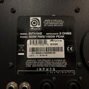Fotografie detailu zadní strany reproduktorové skříně s černým povrchem. Na černé nálepce je logo Ampeg a text: MADE IN THE U.S.A. BY SLM ELECTRONICS…
