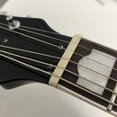 Detail hlavy a hradníku kytary v černé barvě. Na hrazdníku je vidět bílá kostěná nebo plastová matice a vložka z bílého materiálu. Na povrchu jsou vi…