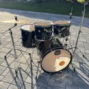Černá bubnová sada značky MAPEX, která obsahuje basový buben, dva tom-tomy a jeden floor tom. Na basovém bubnu je viditelné logo MAPEX a nápis TARAUG…