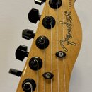 Hlava elektrické kytary z přírodního dřeva s černými ladičkami. Na povrchu je čitelné logo Fender a nápis TELECASTER®. Povrch dřeva vykazuje jemnou s…