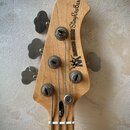 Hlava basové kytary z přírodního dřeva s čtyřmi ladicími kolíky. Na povrchu je černý nápis MUSIC MAN StingRayBass a doprovodné logo s postavou. Povrc…