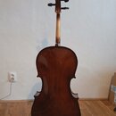 Fotografie zachycuje zadní stranu smyčkového nástroje, pravděpodobně violoncella, v hnědé barvě s lakovaným povrchem. Nástroj stojí na černém stojanu…