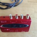 Červený kovový audio interface s čtyřmi RCA konektory. Na přední straně je nápis U-CONTROL, logo výrobce behringer a označení modelu UCA222. Nad kone…
