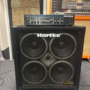 Černý basový reproduktor Hartke s čtyřmi membránami za kovovou mřížkou. V pravém dolním rohu je štítek s nápisem VX series ULTRA PACK a v horní části…