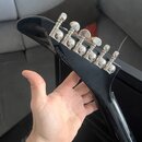 Záběr na černou hlavu elektrické kytary s chromovanými ladicími kolíky. Na zadní straně hlavy je vyrazeno sériové číslo 24091523570. Povrch laku je h…