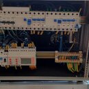 Otevřený hliníkový transportní kufr s montovaným rozváděčem elektrických jističů. V horní a spodní části jsou na lištách upevněny bílé moduly jističů…