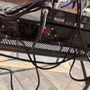 Zadní strana černého rackového zesilovače s kovovým šasi a ventilační mřížkou. Jsou zde viditelné nápisy OUTPUT CONNECTIONS, INPUT CONNECTIONS, EARTH…