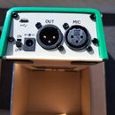 Záběr na zadní panel zelenobílého elektronického zařízení. Jsou zde vidět konektory USB-C, XLR označený jako OUT a XLR označený jako MIC, dále přepín…