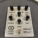 Stříbrný efektový pedál s nápisem AUDIO EVENT a DREAMY DELAY. Na horní straně se nachází šest černých otočných knoflíků s popisky delay time, speed,…