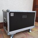 Černý transportní case s hliníkovými hranami a kovovými rohy, osazený kolečky. Na přední straně je bílý nápis REVV a v horním levém rohu nálepka s te…