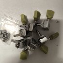Sada šesti ladících kolíků s kovovými mechanismy a plastovými knoflíky v olivové barvě. Kolíky jsou rozprostřeny na světlém povrchu, vedle nich je pr…