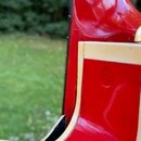Detail červené kytary s bílým lemováním hran. Je vidět spojení krku s tělem nástroje a část hmatníku. Povrch laku je lesklý, v místě spoje jsou vidit…